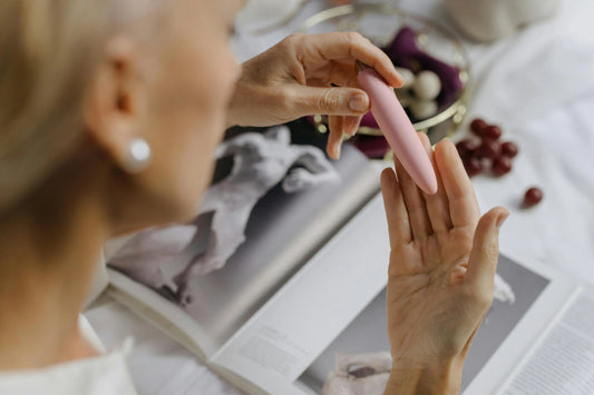 Woman holding a pink bullet vibrator demonstrating how to use a bullet vibrator with a book in the background